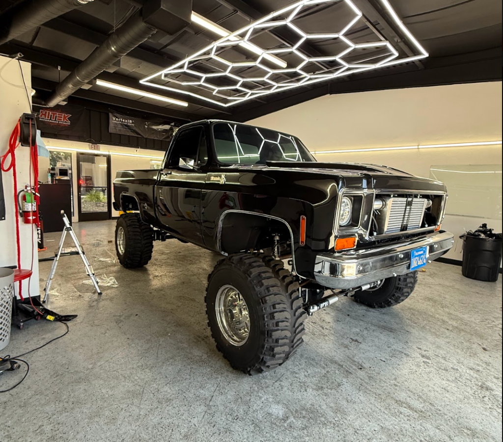 Lifted classic black pickup truck with chrome trim and off-road tires inside the Royal Window Tint shop