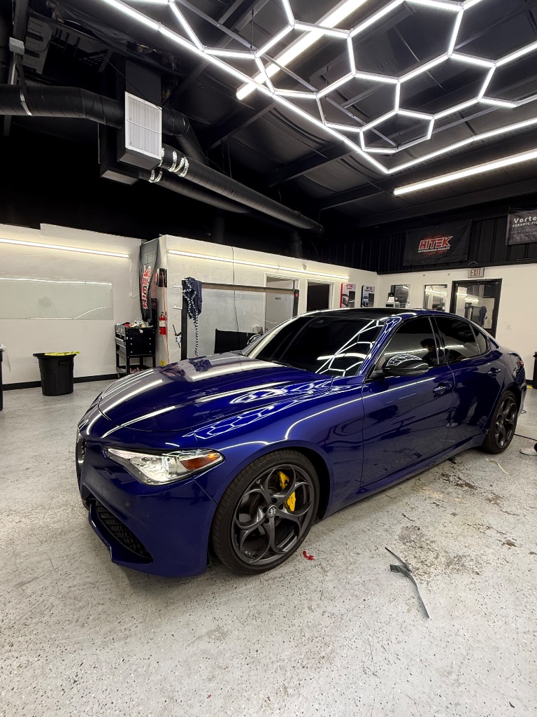 Deep blue Alfa Romeo sedan with tinted windows inside the Royal Window Tint shop