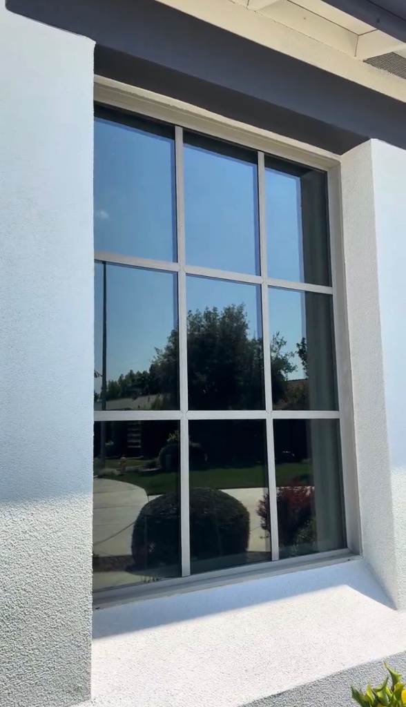 Residential window with reflective tint film on a white stucco home exterior