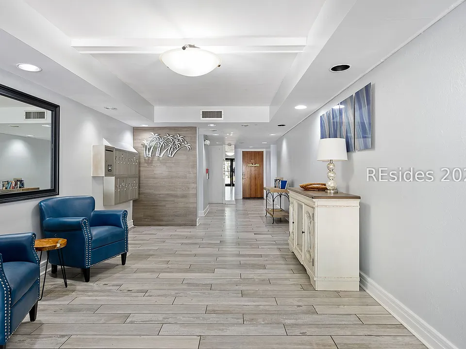 Elegant building lobby of the Monterey on Hilton Head Island with navy armchairs, a framed mirror, brass mailboxes, and coastal art above an off-white console
