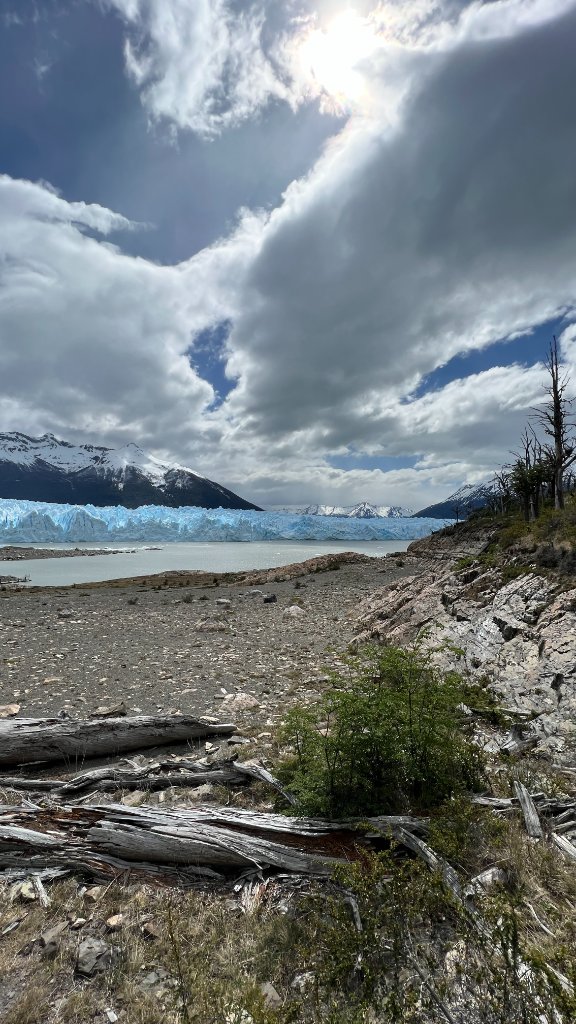 Glacier and dramatic clouded sky over a rocky shoreline