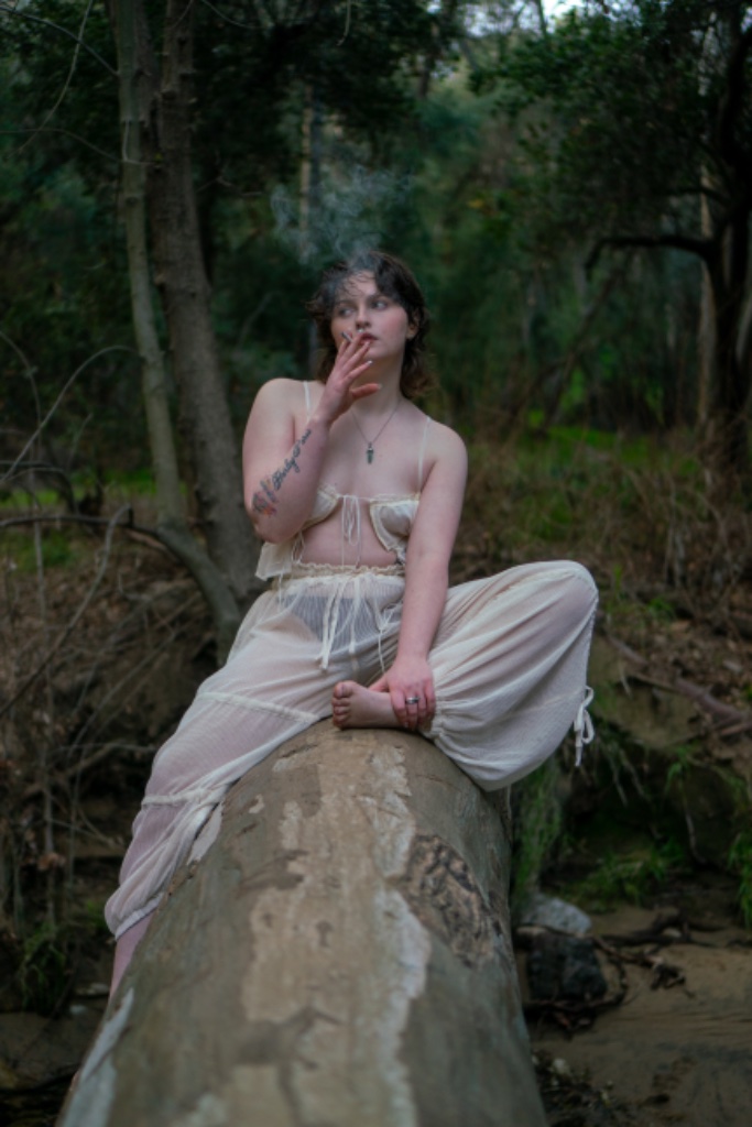 Person sitting on log in forest, sheer off-white two-piece outfit