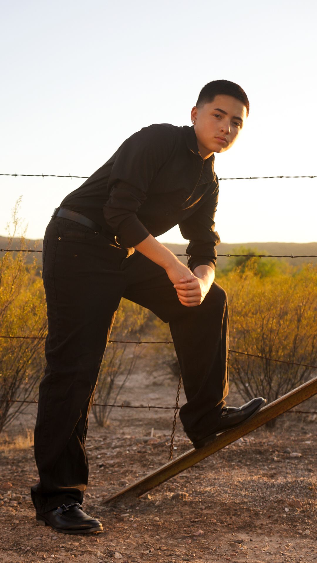 Young man leaning on fence post in desert at sunset
