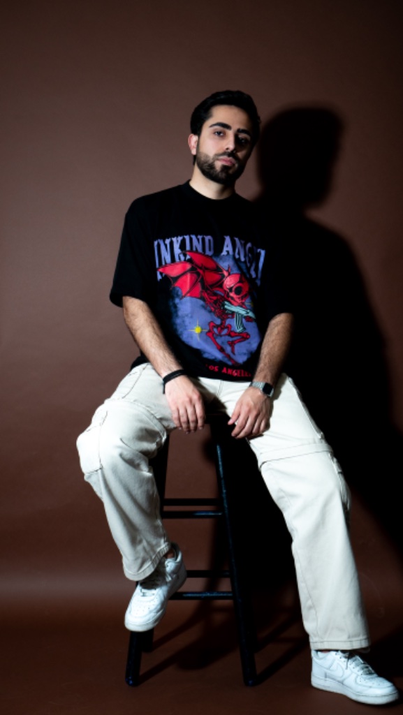 Male model seated on stool in black graphic tee, dark studio background