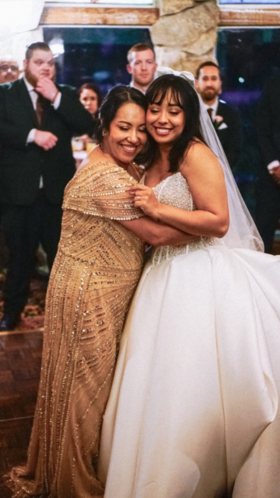 Bride embracing woman in shimmering gold gown at wedding reception