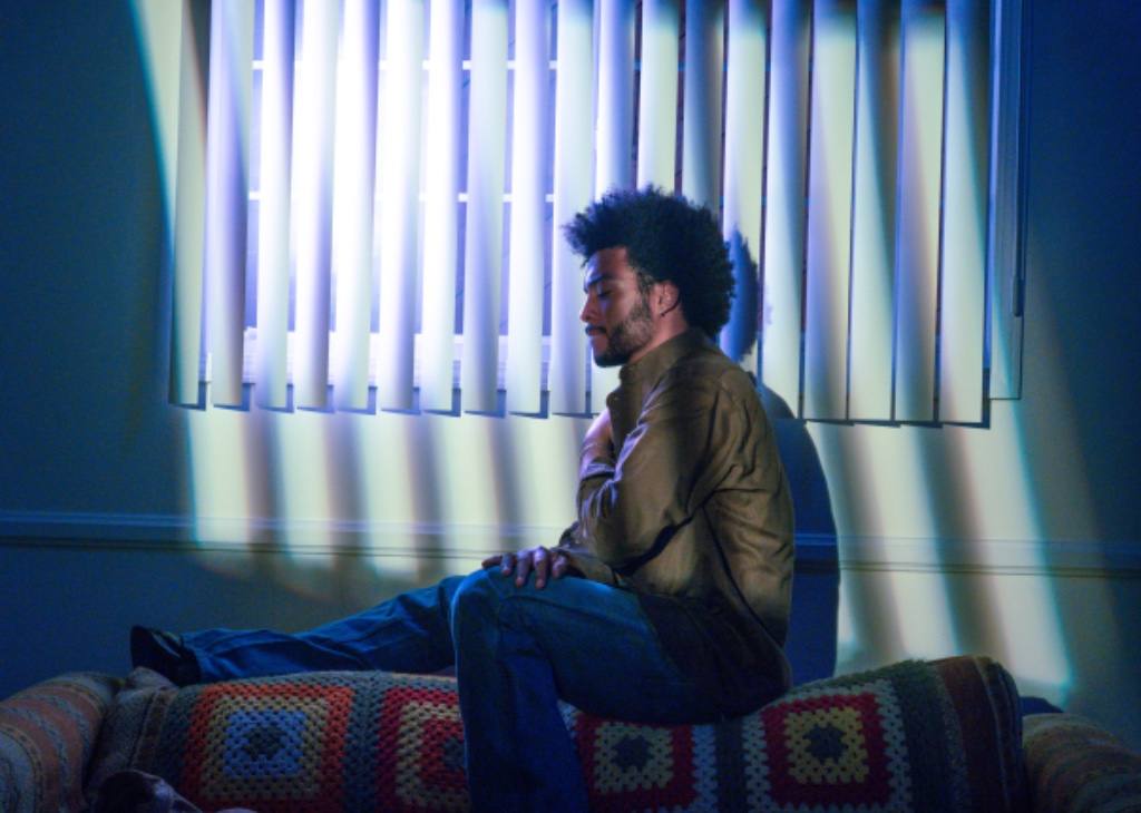 Felix Ames on crocheted couch with vertical blind shadows