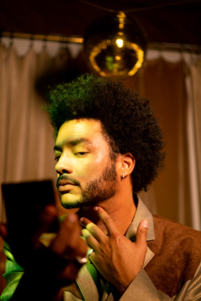 Felix Ames in brown jacket hand to neck, disco ball and green light streak