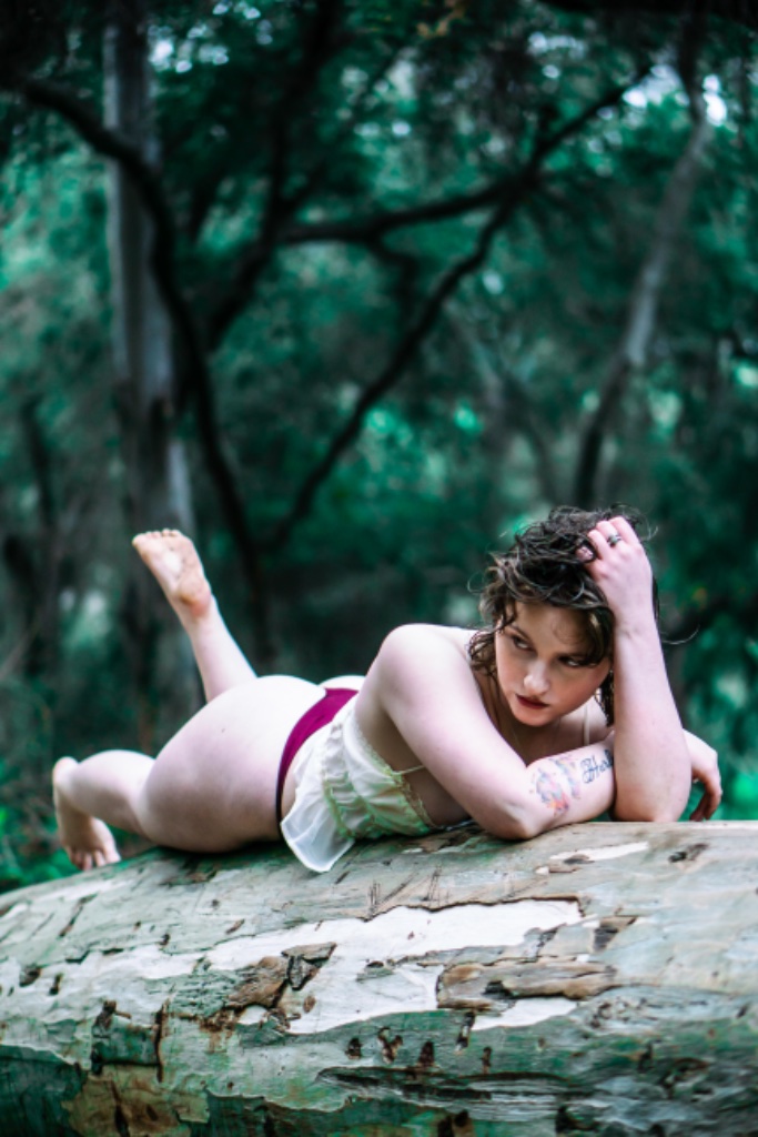 Woman lying on stomach on log, head on hand, leg bent upward