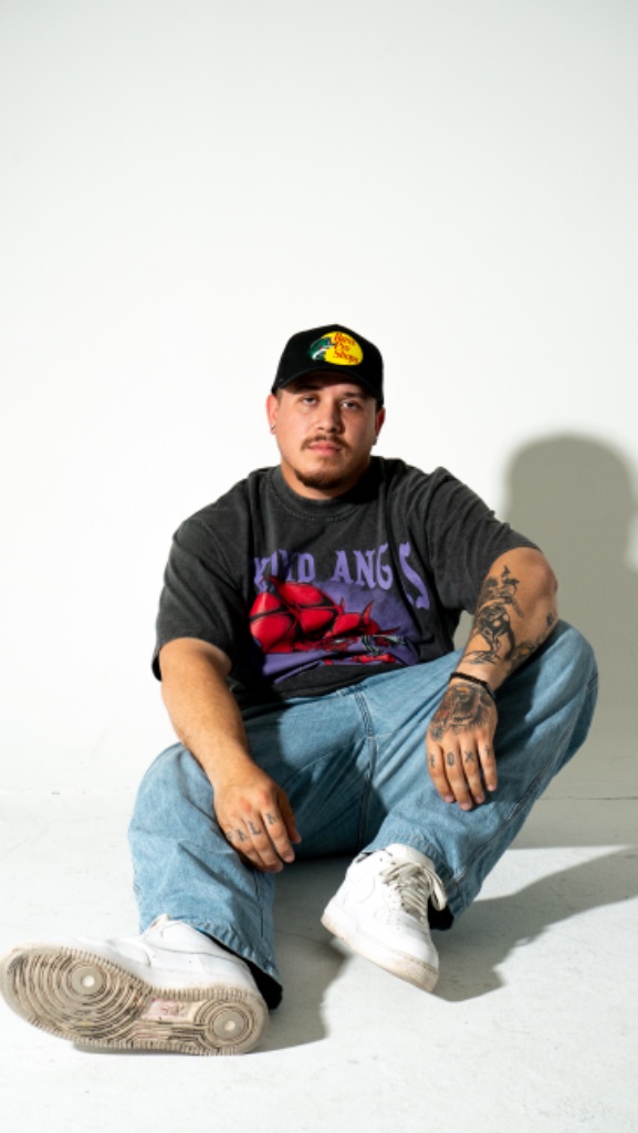 Male model seated on floor in graphic tee and jeans, white studio backdrop