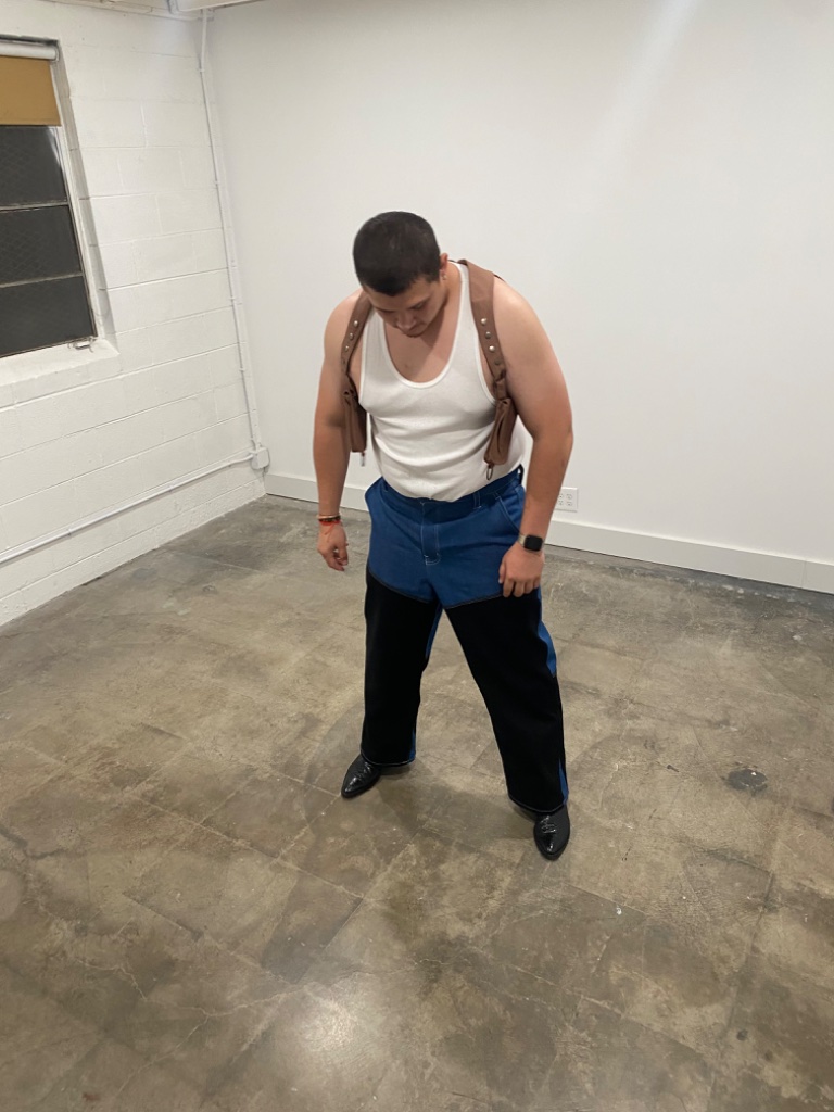 Man in white tank top and leather harness with two-tone jeans, studio setting
