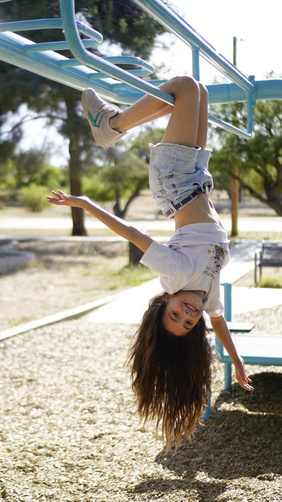 Girl hanging upside down on playground bars, smiling, by Jose A. Palafox