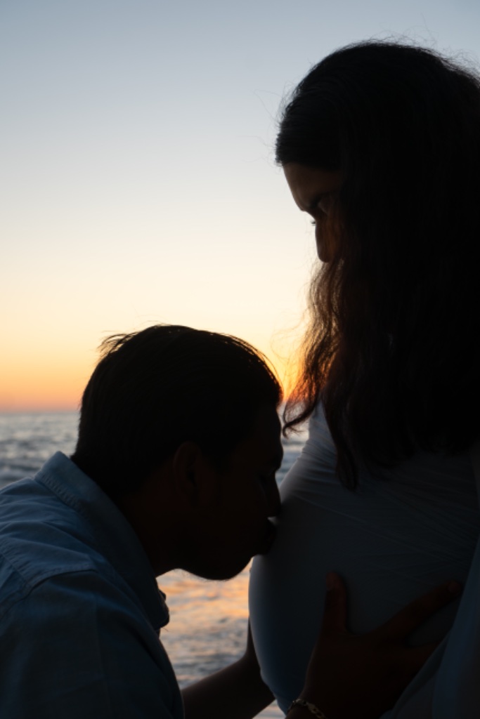 Man kissing baby bump at sunset, silhouette on the beach