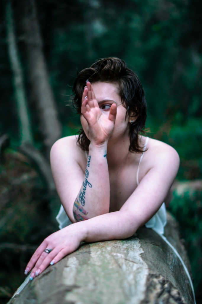 Woman resting on log with hand covering eyes, Harley Paris tattoo visible