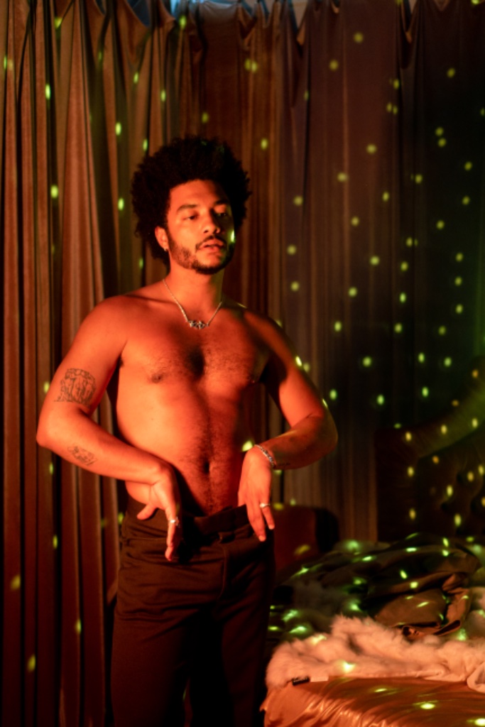 Felix Ames shirtless with green disco ball light dots on curtains