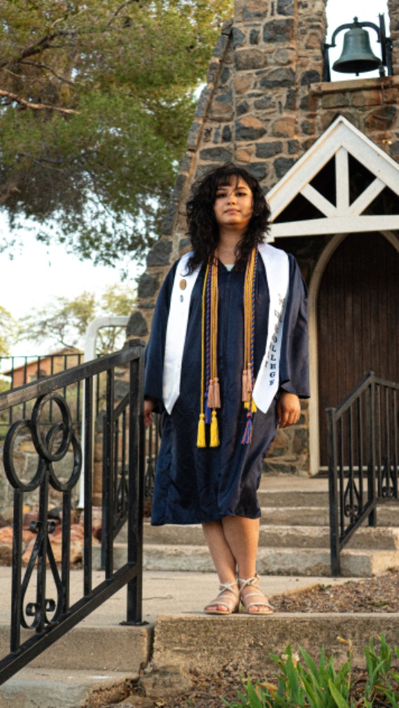 Full-body portrait of graduate on concrete steps with stone building and bell