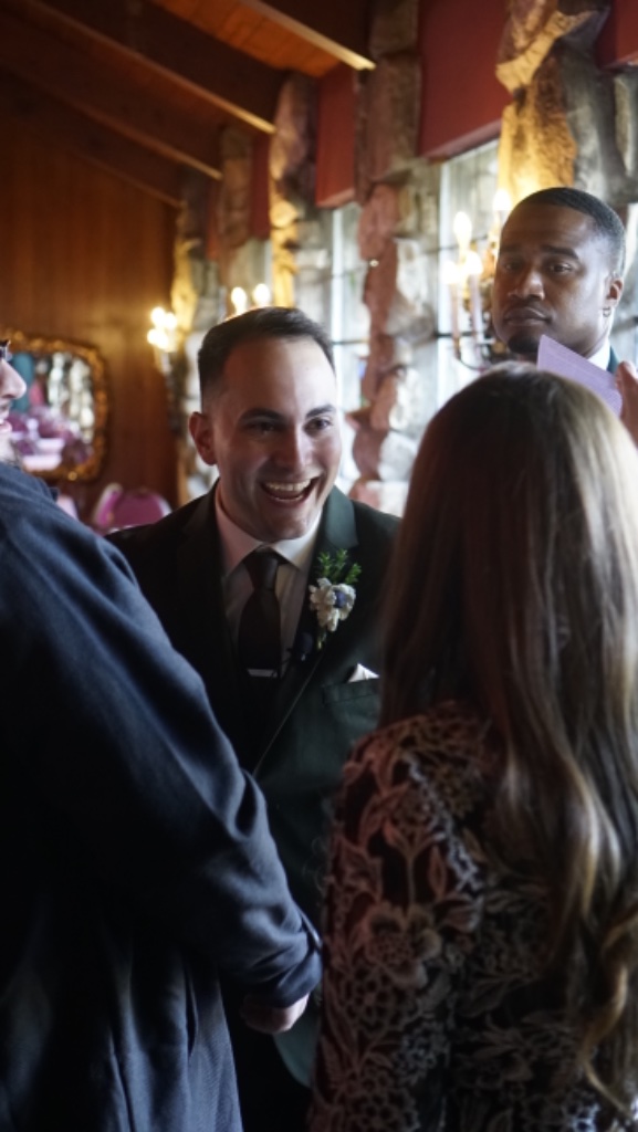Groom in olive green suit smiling joyfully at bride during wedding reception