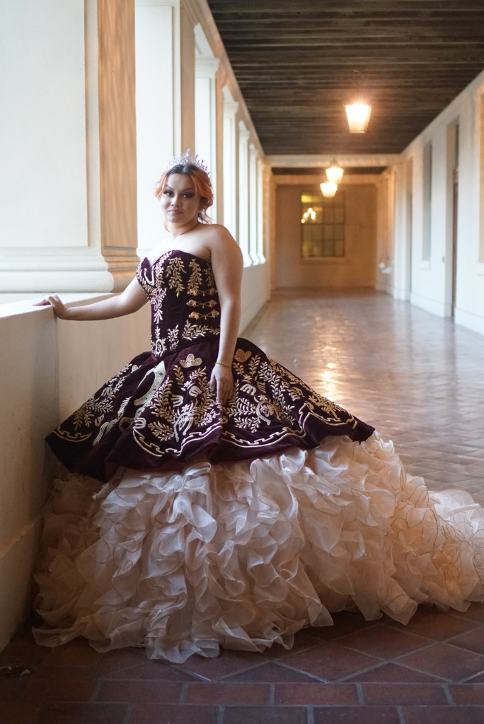 Quinceañera in embroidered gown leaning against a column in a historic hallway