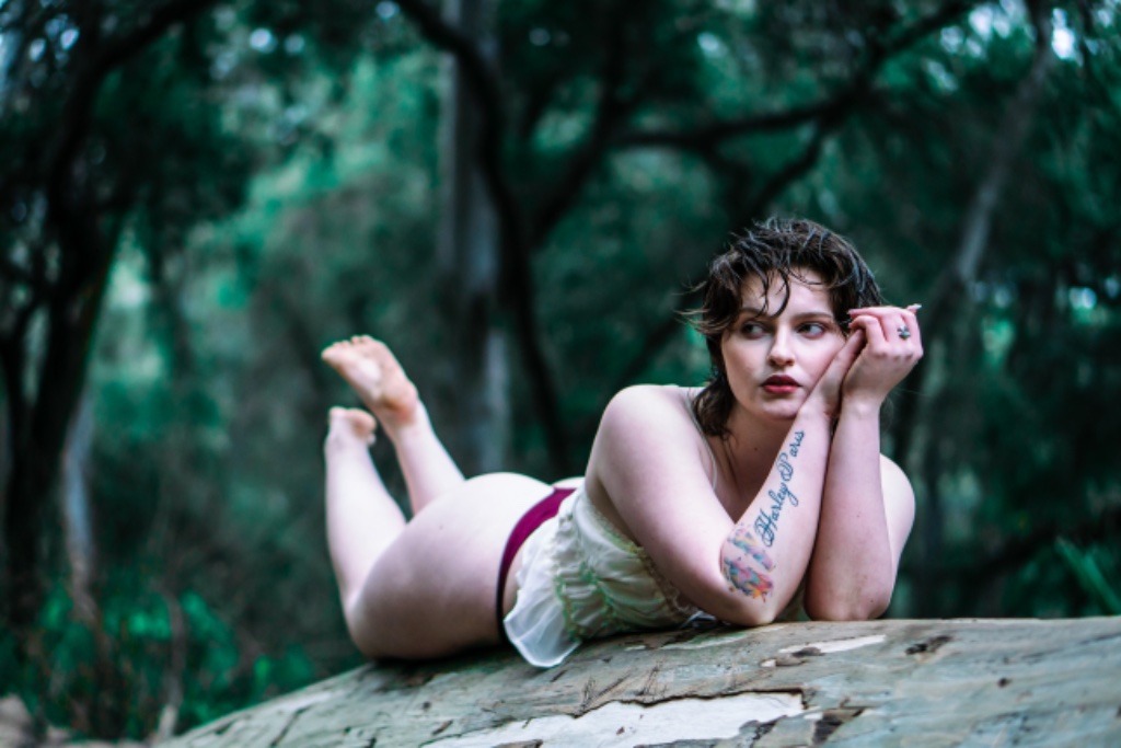 Woman lying on stomach on tree log, legs raised, forest background
