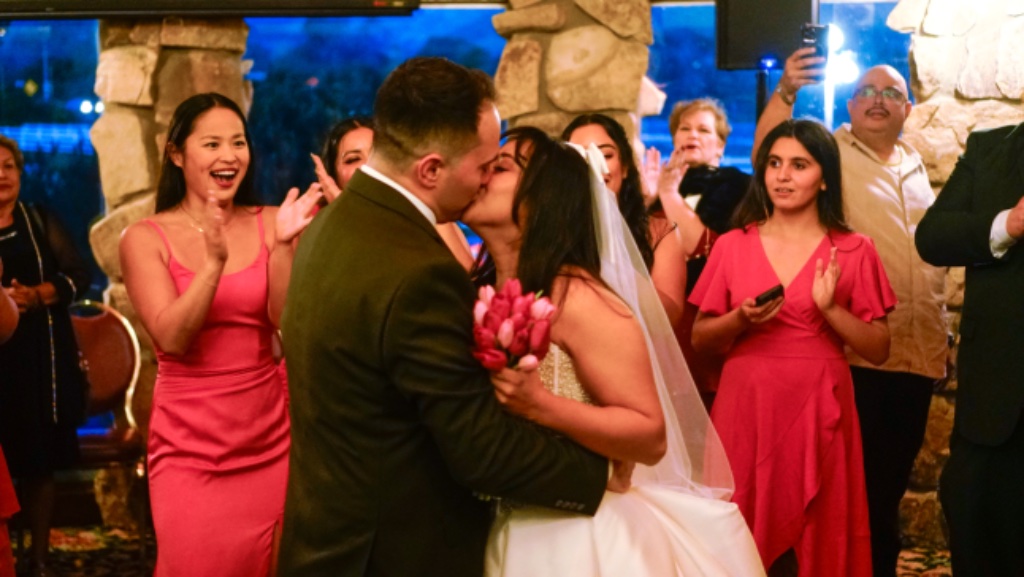 Bride and groom first dance surrounded by guests in pink dresses at wedding reception