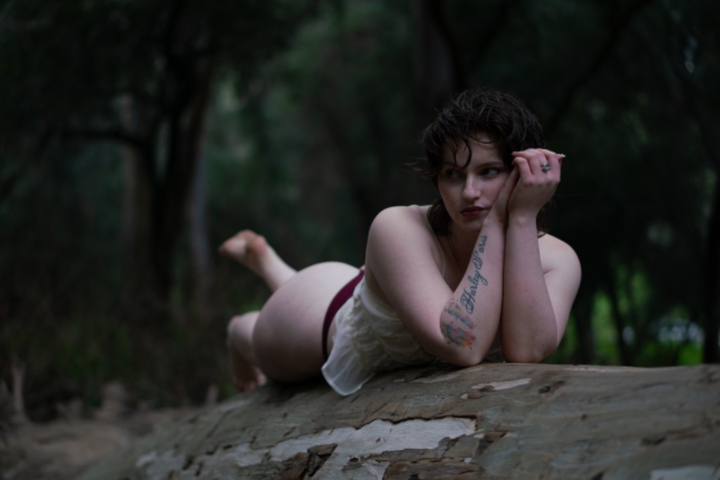 Person resting on tree trunk in forest, Harley Paris tattoo visible