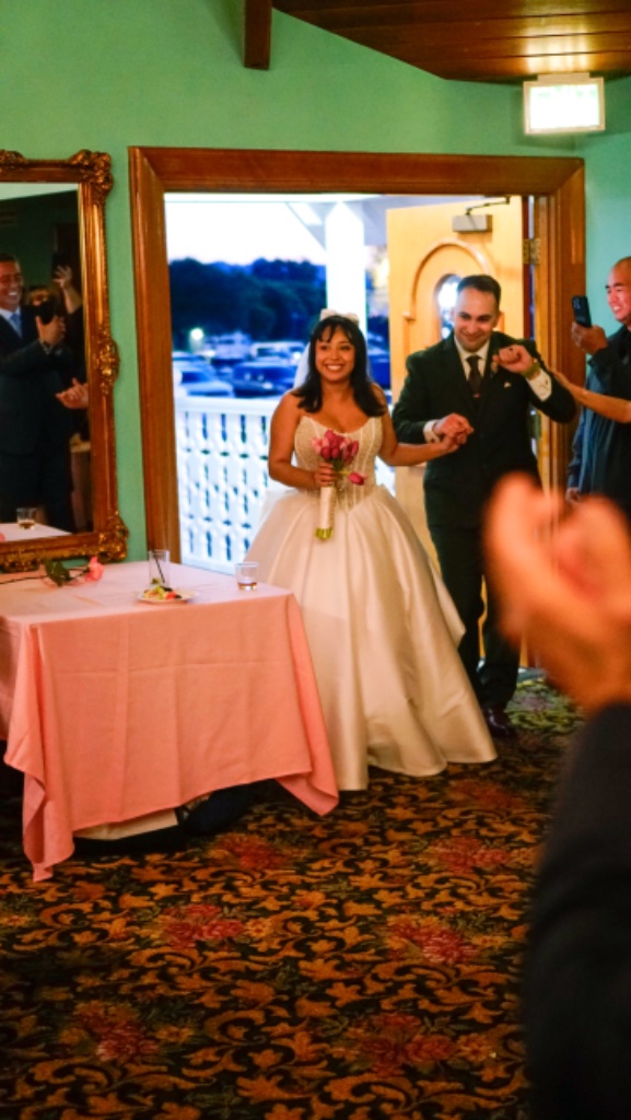 Bride in white ballgown and groom in olive suit walking hand-in-hand through doorway at reception