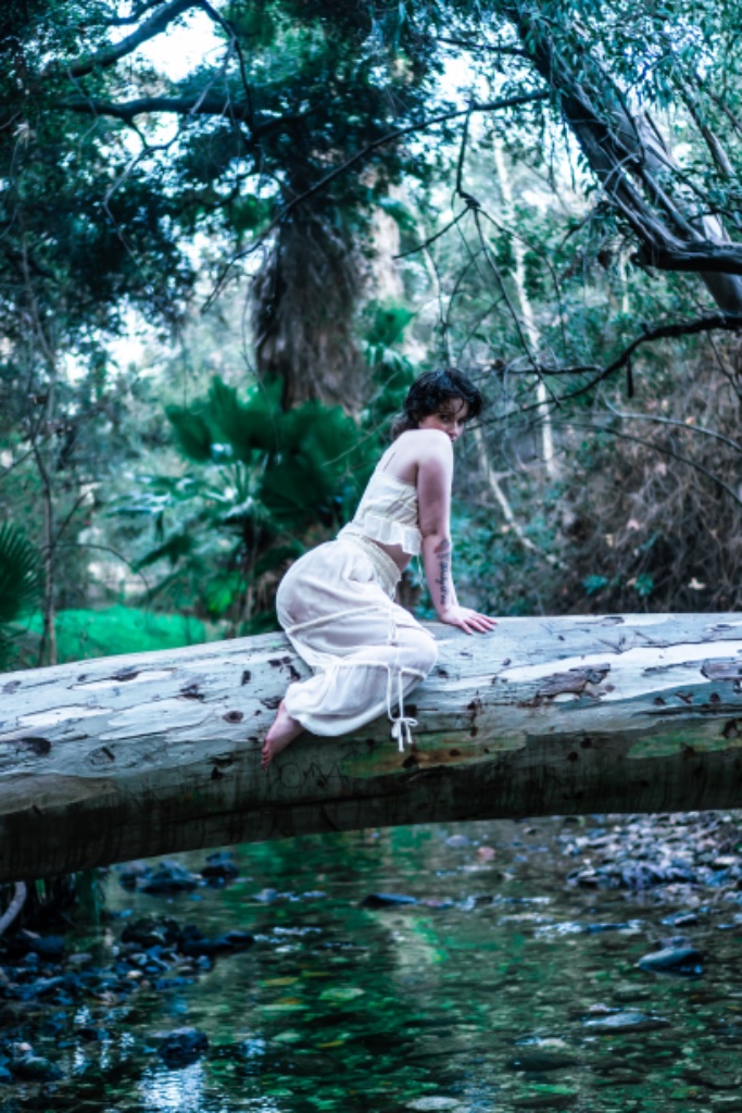Woman sitting on log facing away, looking over shoulder at camera