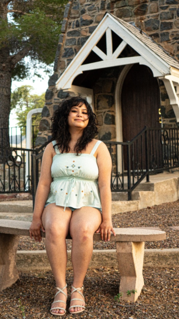 Graduate in sage green top seated on stone bench in front of stone building