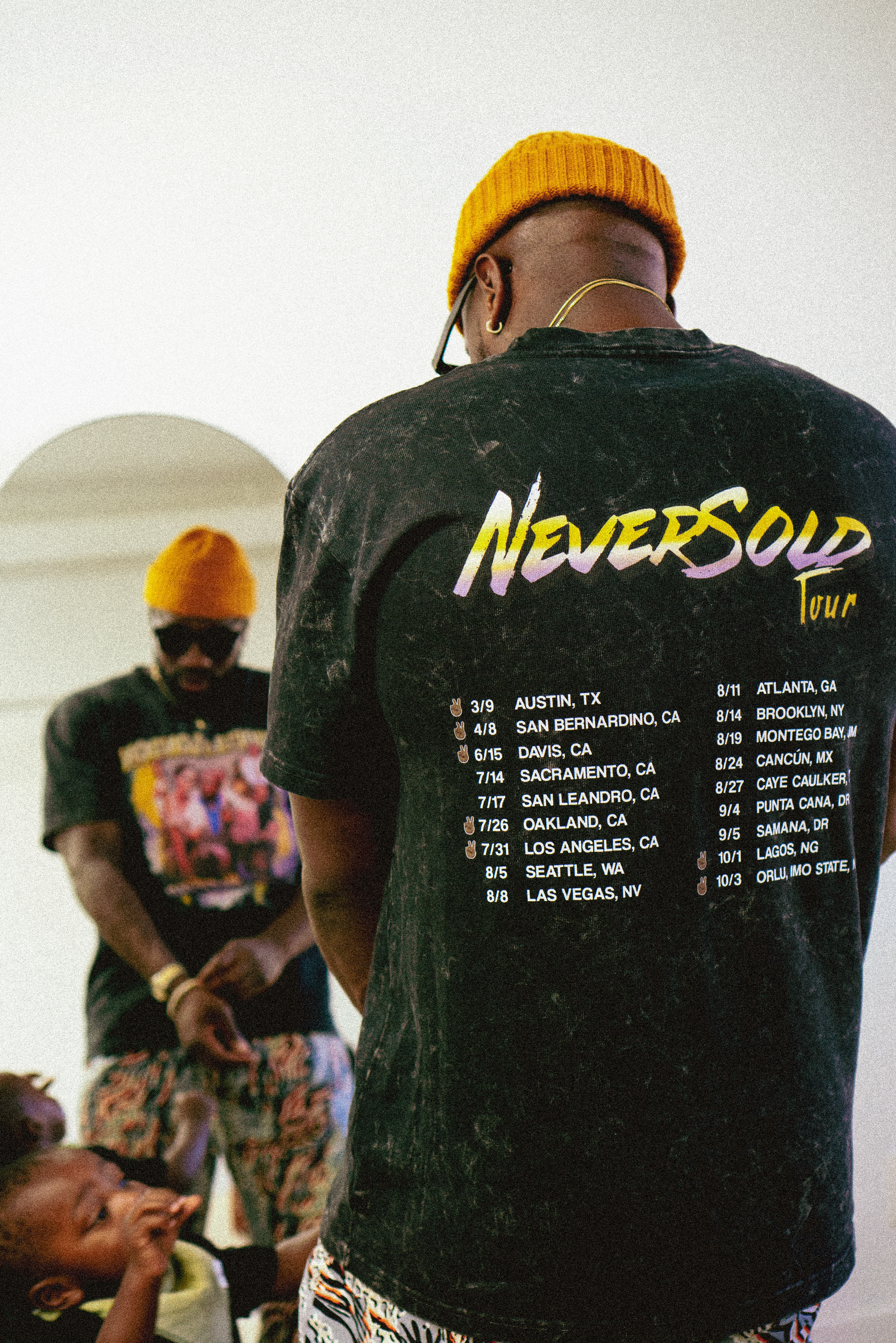 Man in NeverSold Tour tee and yellow beanie, back to camera in studio