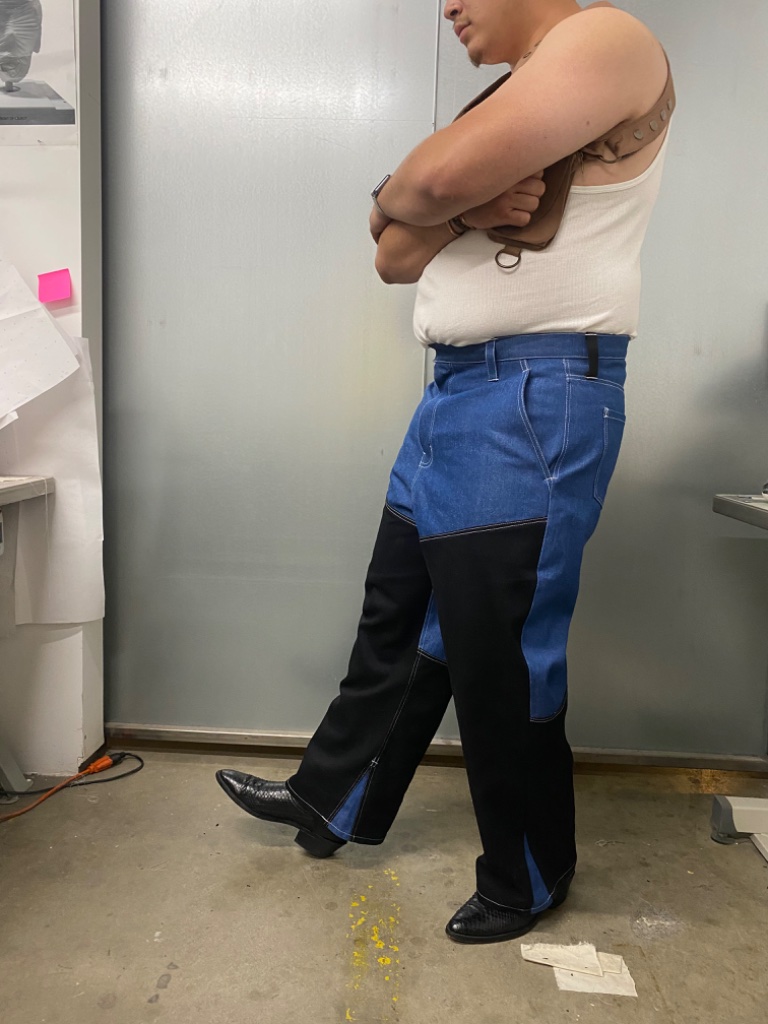 Man in white tank top and leather harness with two-tone pants, profile pose