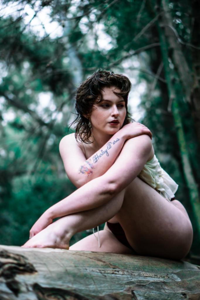 Woman sitting on fallen tree log, arms crossed, looking away in forest setting