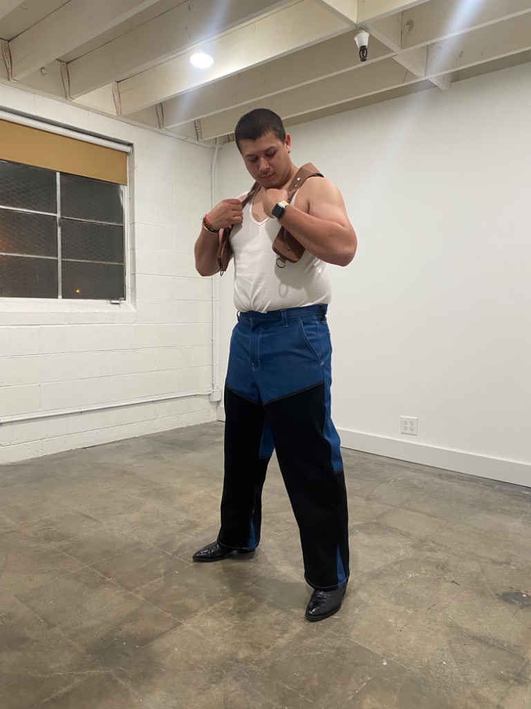 Man in white tank top and leather harness with two-tone jeans, studio portrait