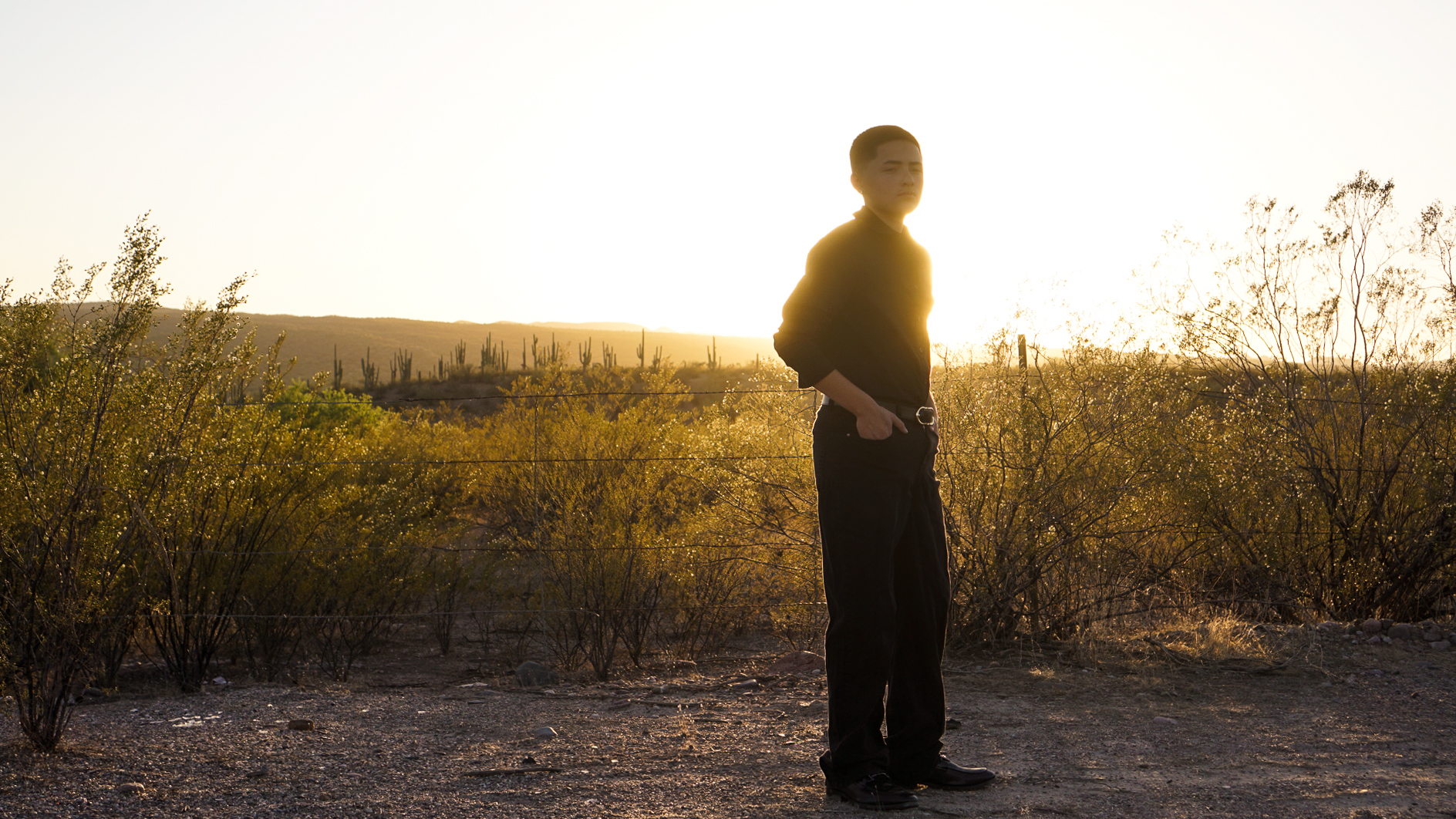 Young man standing in desert at dusk, backlit by warm golden light