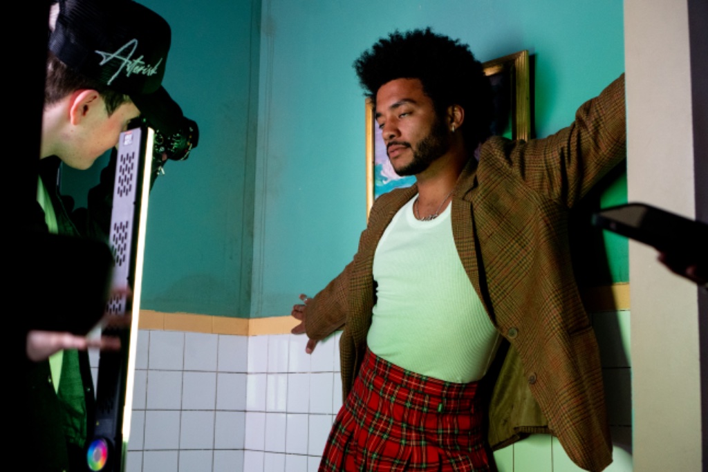 Felix Ames in plaid blazer and skirt against turquoise wall with photographer