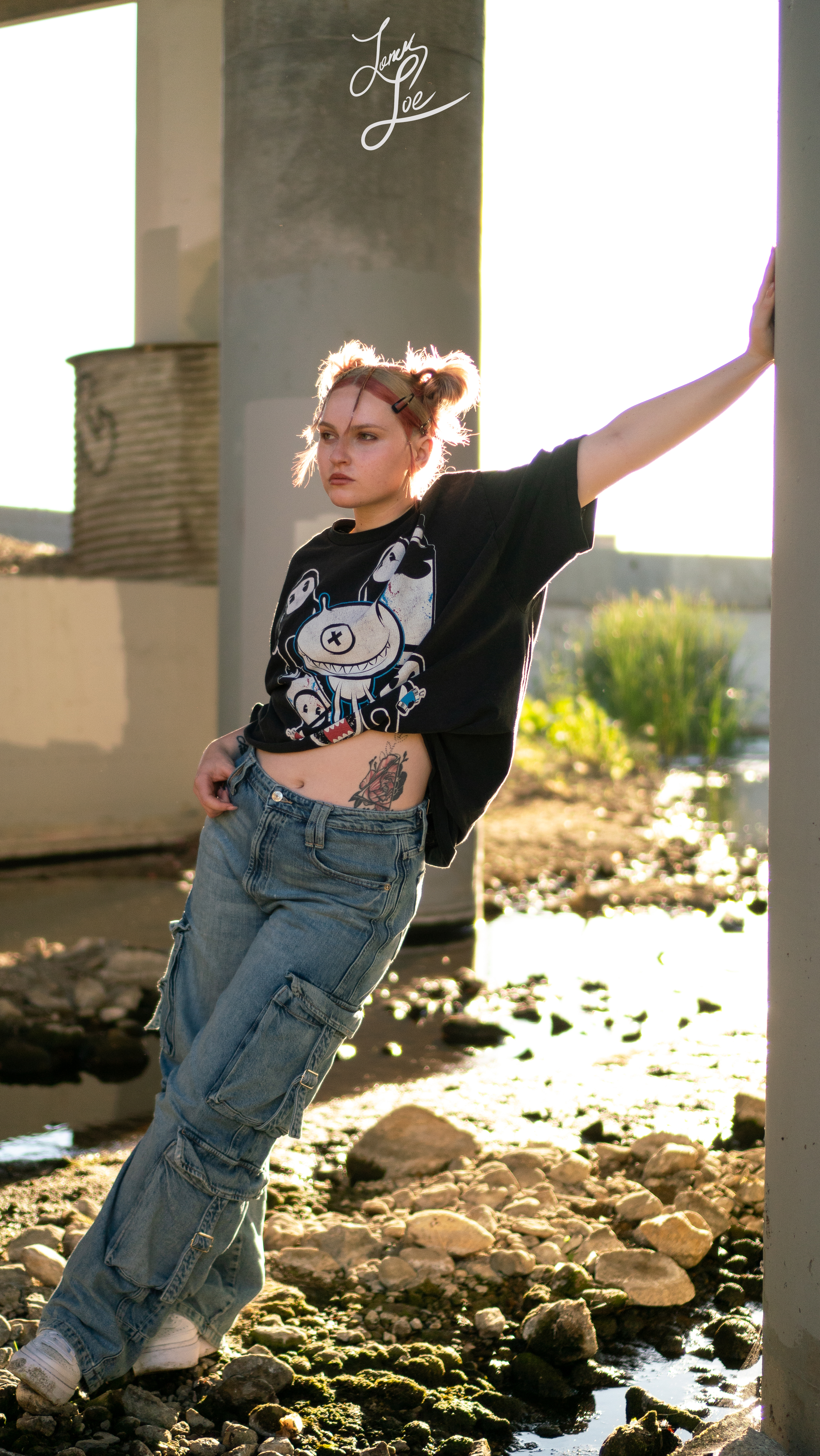 Woman leaning on pillar in graphic tee and cargo jeans, urban riverbed setting