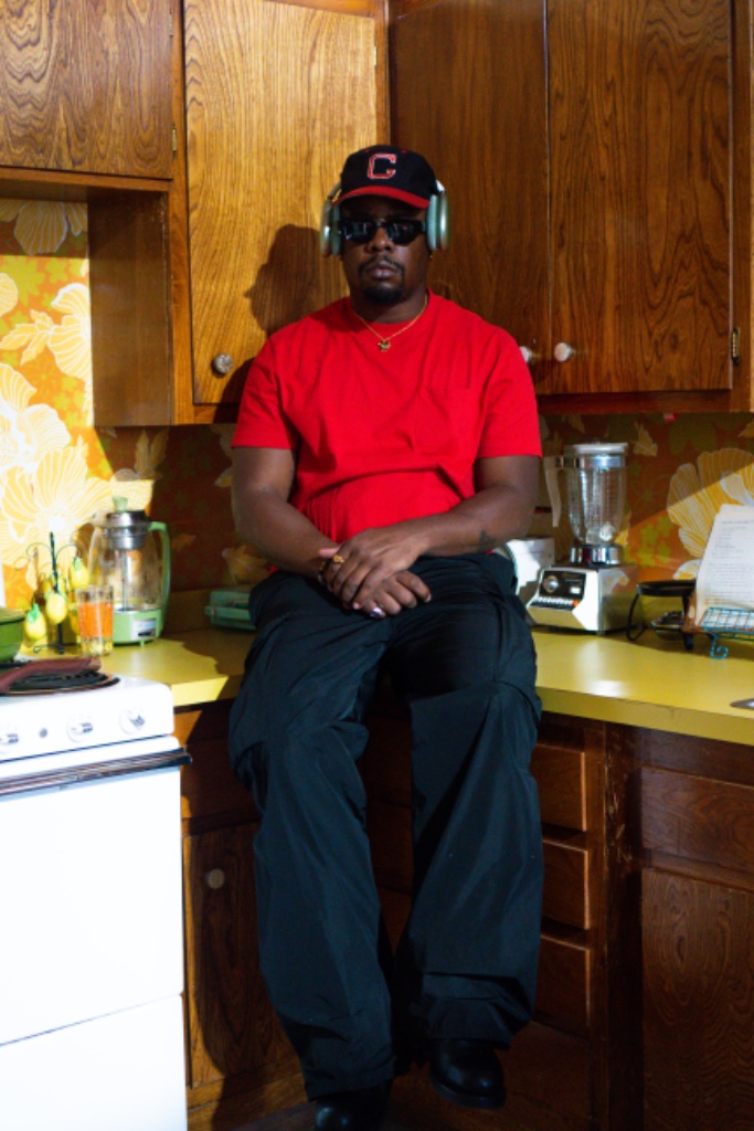 Felix Ames in red tee and cap with headphones on kitchen counter