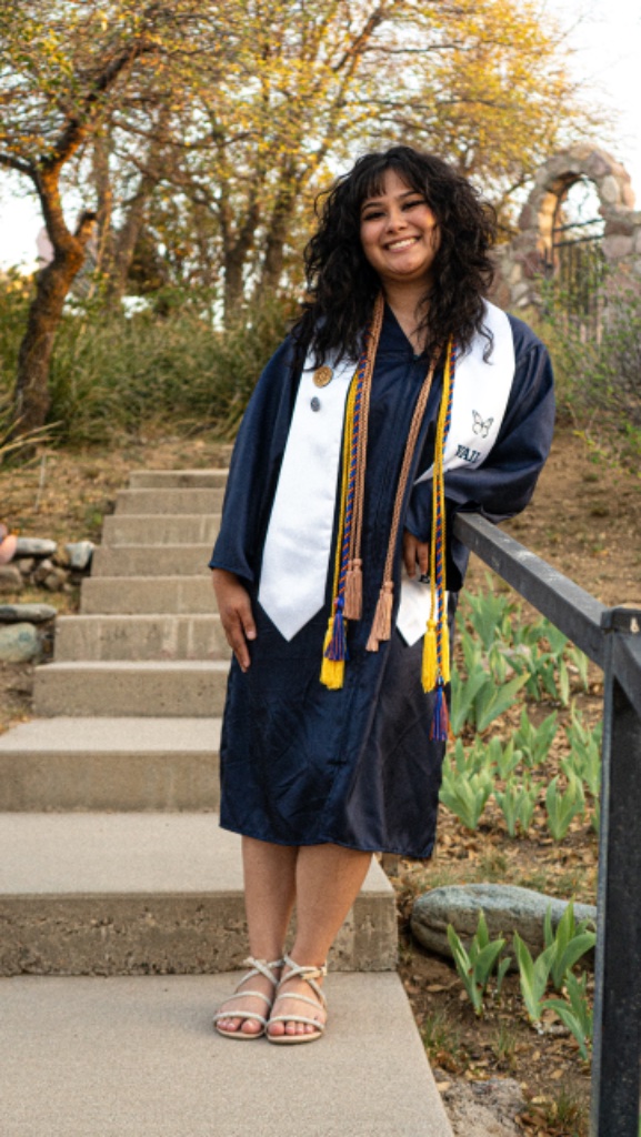 Graduate leaning on metal railing on concrete stairs with stone building background