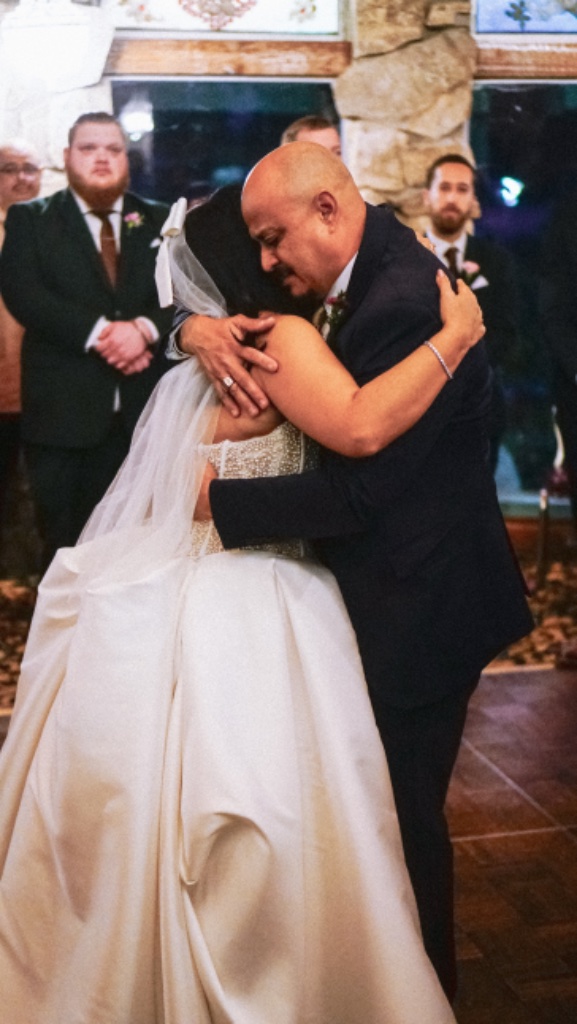 Bride embracing older man with mustache in dark suit on dance floor