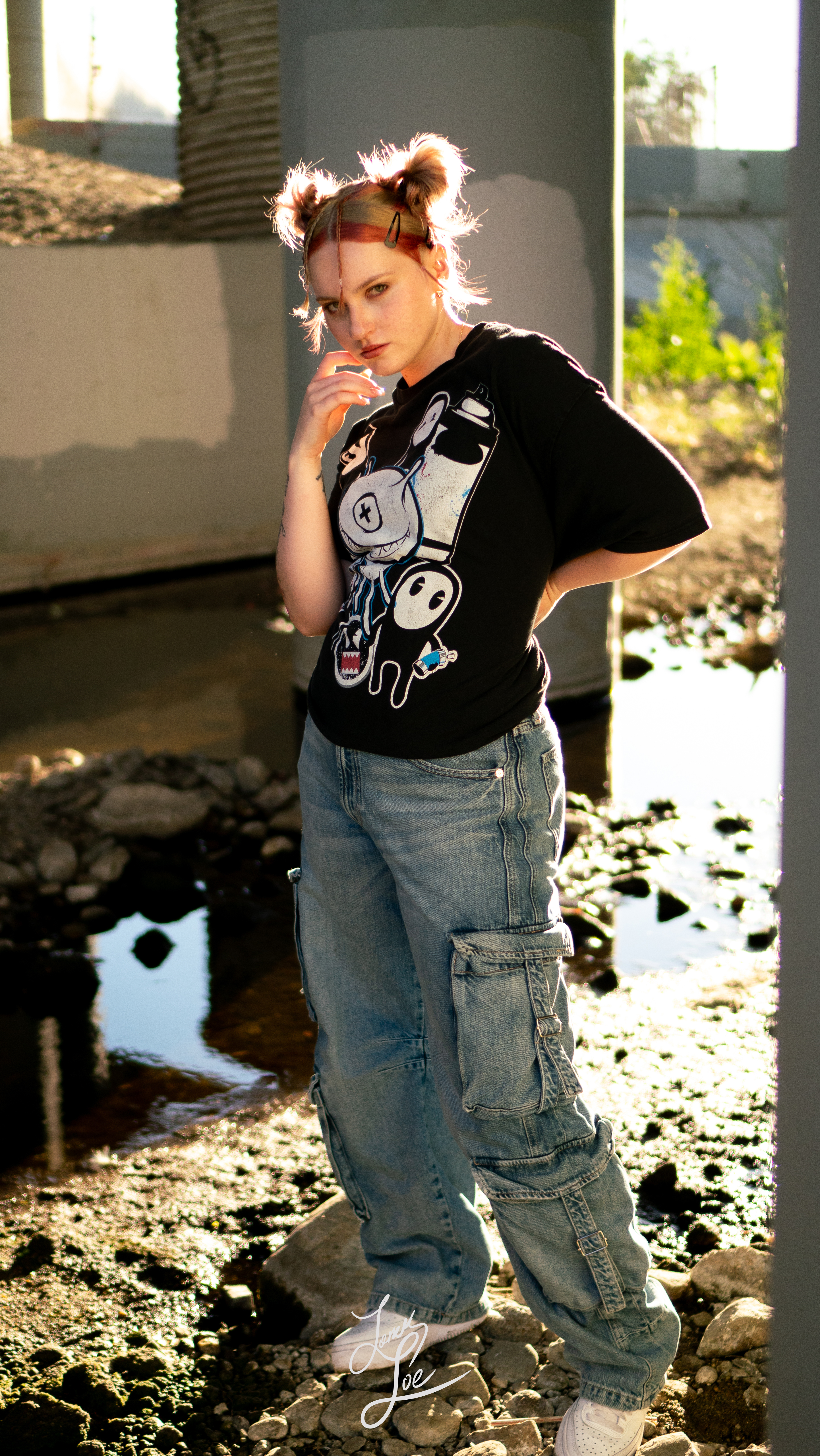 Woman in graphic tee and cargo jeans posing under bridge at golden hour