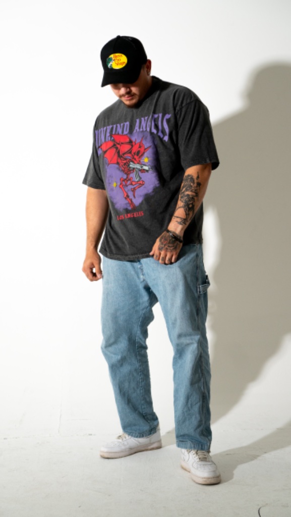 Tattooed male model in graphic tee looking down, white studio backdrop