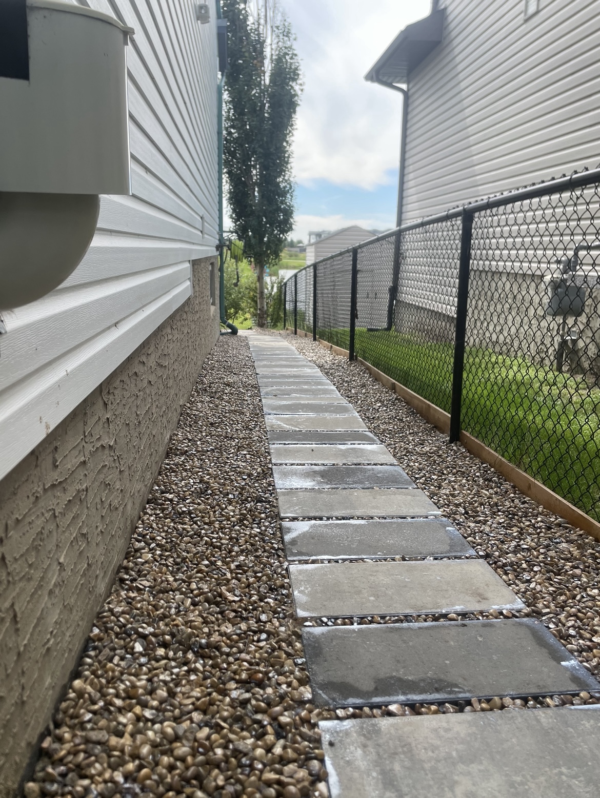 Linear gray concrete pavers set in decorative gravel, running clean between the house and fence to the backyard