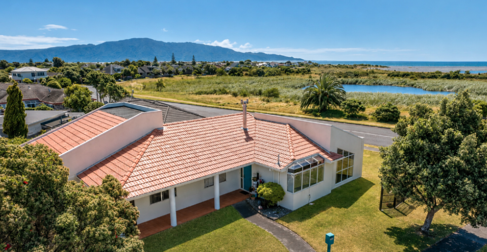 Single-story white home with terracotta roof, porch pillars and coastal dune views