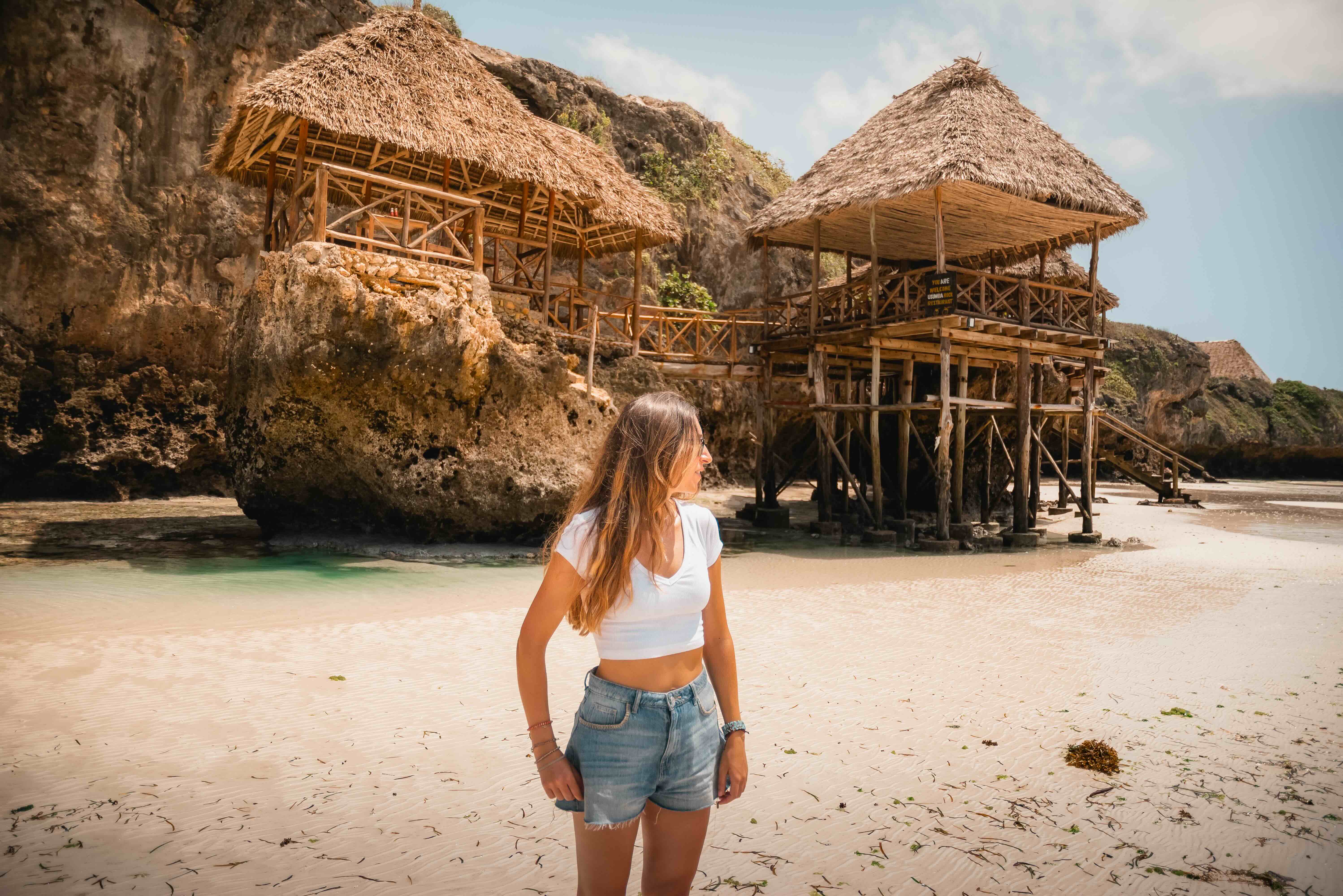 Tourist walking on a beach admiring rocky shoreline and palm huts