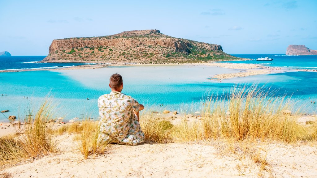 Traveler sitting on a dune overlooking a turquoise lagoon