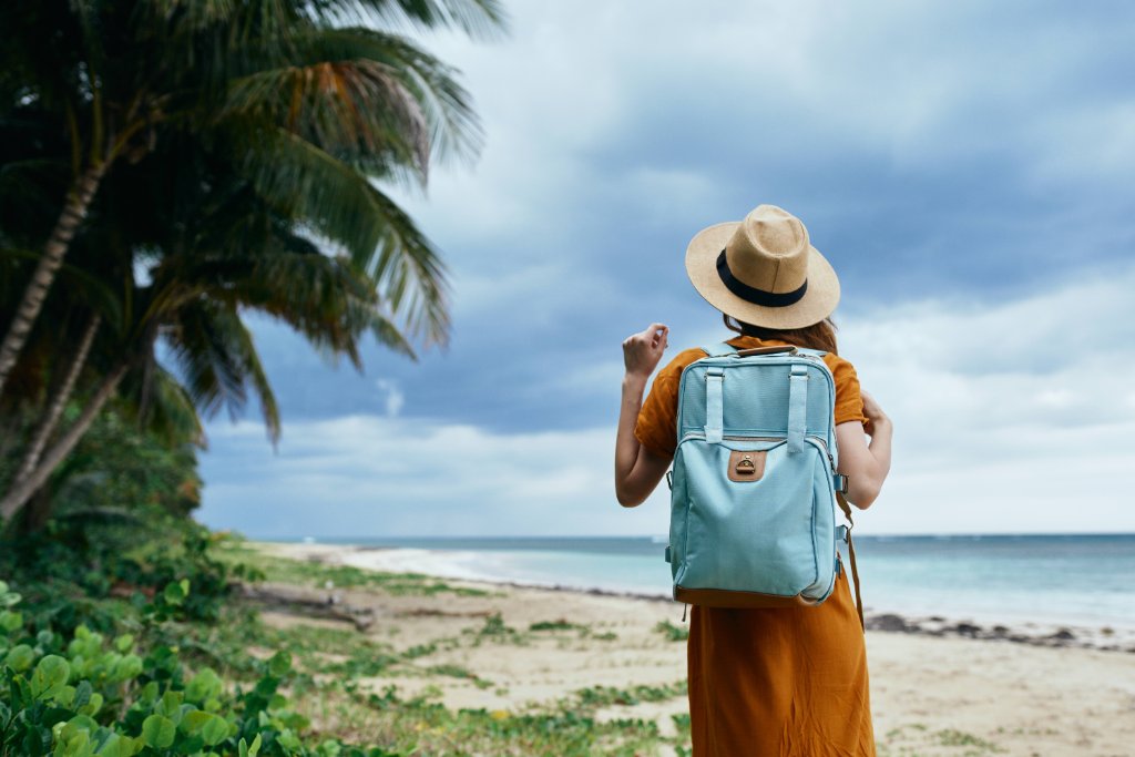 Traveler with backpack and hat on a palm-lined beach