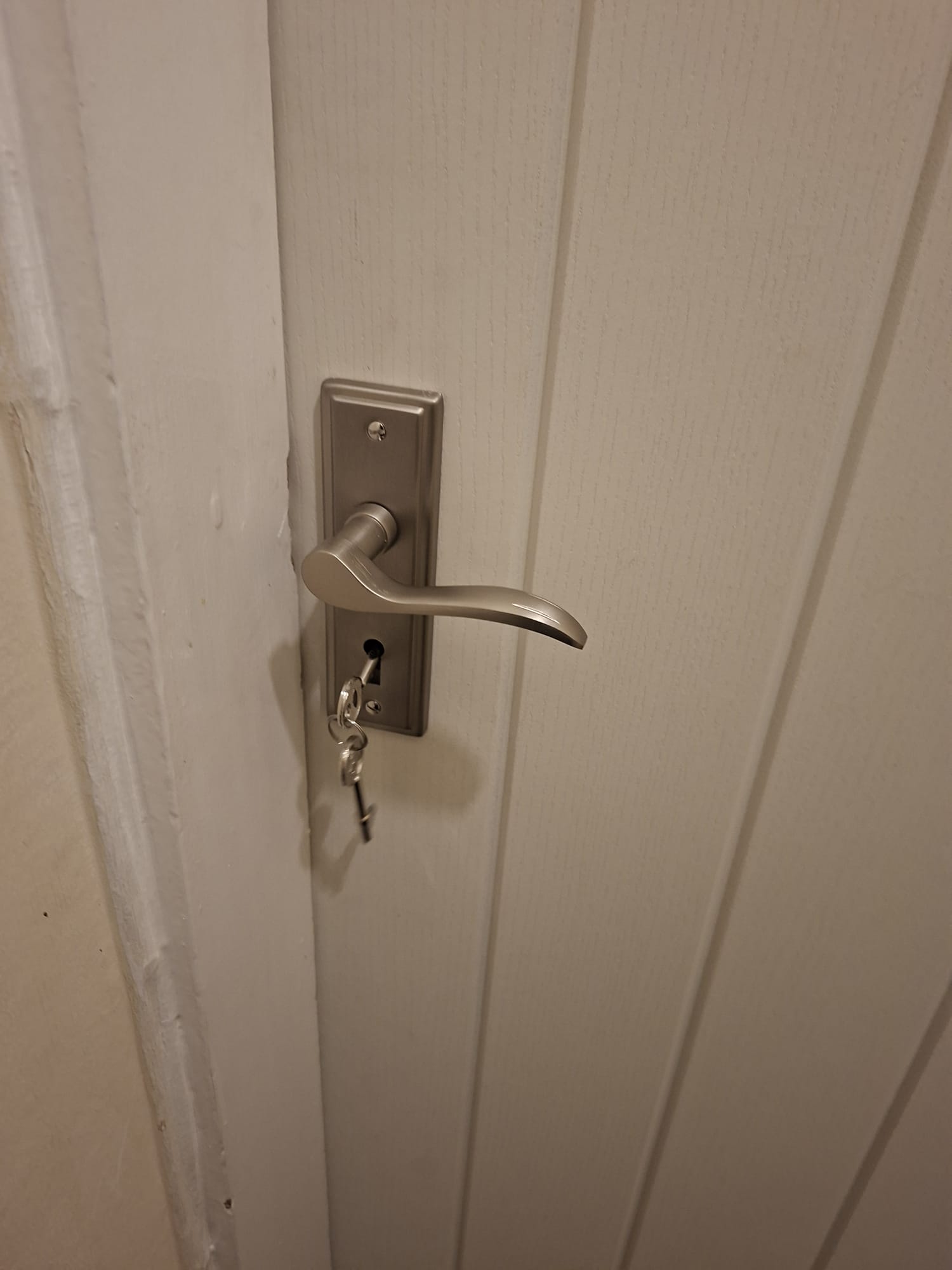Brushed nickel lever door handle with a key inserted in the lock on a white paneled door in Hampton, Peterborough