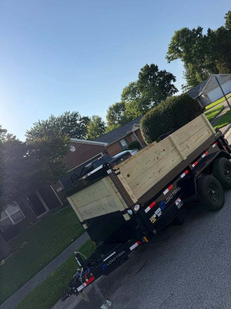 Rear-three-quarter view of Load Trail dump trailer hitched to a pickup truck