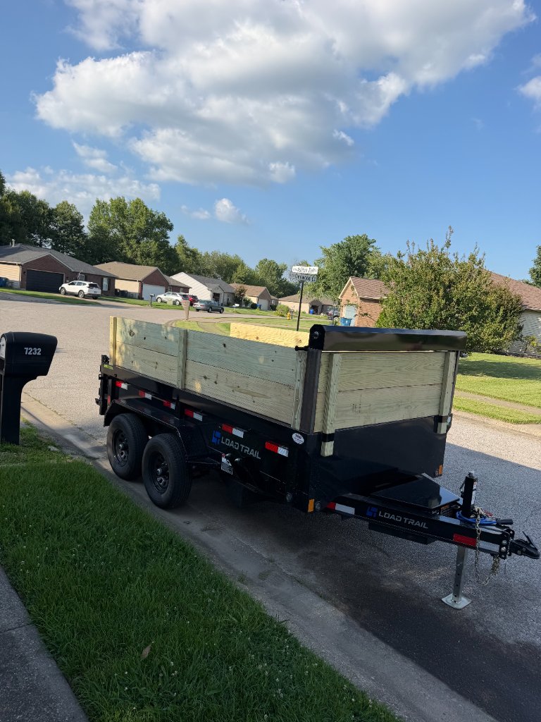 High-angle side-rear view of black Load Trail dump trailer with wooden side boards