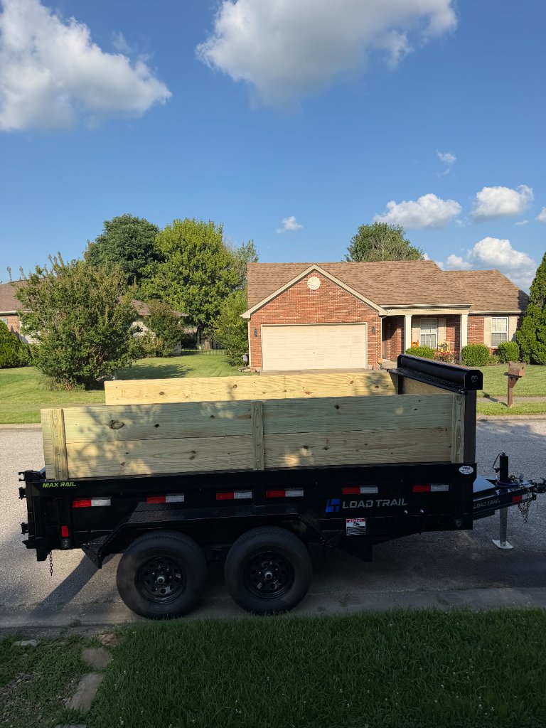 Side profile of Load Trail dump trailer with wooden side extensions parked on a residential street