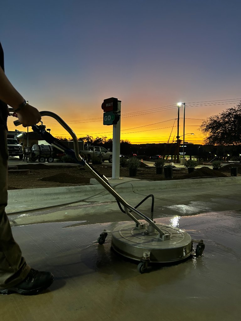Pressure washing technician surface cleaning concrete at golden hour sunset in Austin
