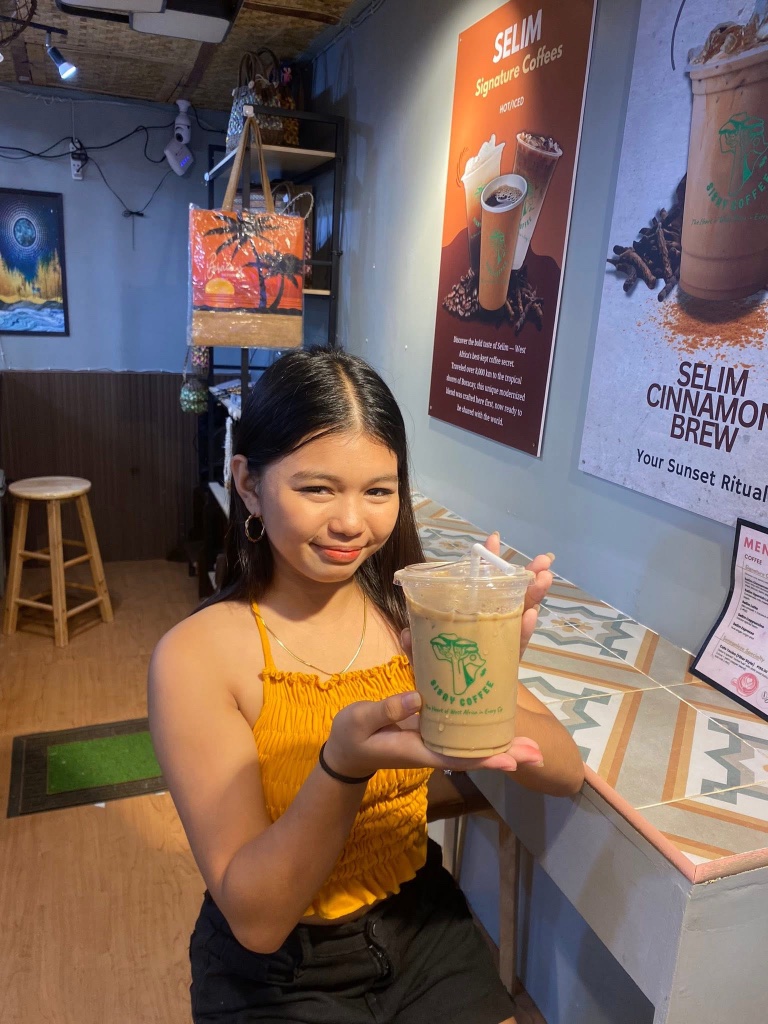 Smiling customer holding an iced Sisay Coffee at the shop counter